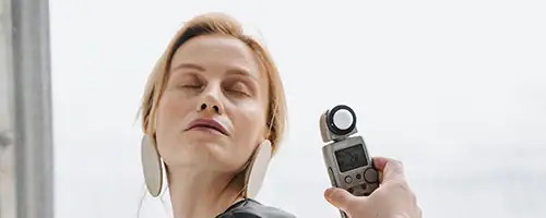 A person with closed eyes faces a handheld light meter being held up to their face against a bright, neutral background, illustrating a scene typical in professional studio hire Canberra settings.