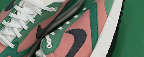 Close-up of a pair of sneakers with pink, green, and white panels, white laces, and a black Nike swoosh logo on a green background—perfect for your next shoot or studio hire Canberra session.